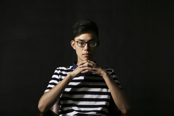 Ein junger, asiatisch aussehender Mann in gestreiftem Shirt und mit Brille.