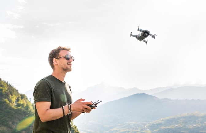 Ein Mann steuert eine Drohne fern. Im Hintergrund sieht man Berge.