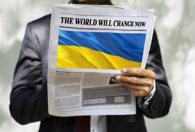 Ein Mann liest eine Zeitung. Auf dem Titelbild ist eine ukrainische Flagge abgebildet, darüber steht: Die Welt wird sich jetzt verändern.