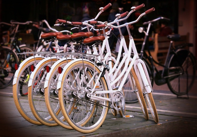 4 identische weiße Fahrräder stehen nebeneinander, im Hintergrund sieht man weitere Räder.