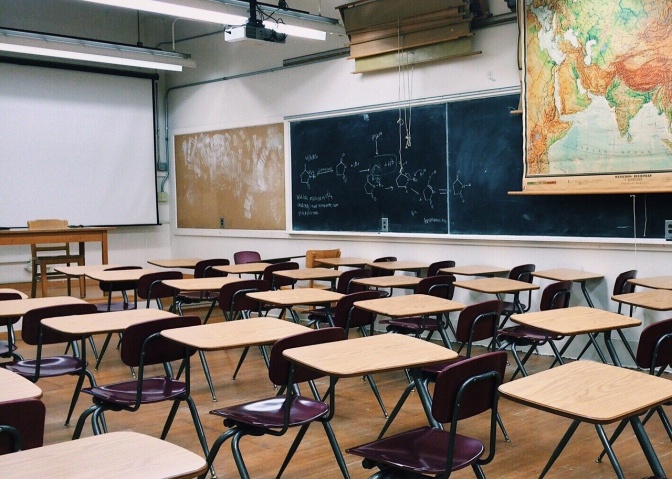 Ein leeres Klassenzimmer mit kleinen Tischen und Stühlen. An der Wand hängen Tafeln und eine Landkarte.