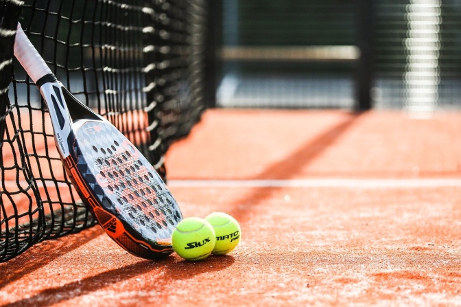 Ein Tennisschläger lehnt am Netz, davor liegen 2 Tennisbälle.