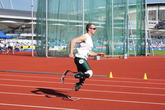Ein Läufer mit Prothesen ab dem Oberschenkel. Er läuft über eine Rennbahn in einem Stadion.