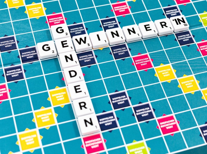 Auf dem Scrabblefeld sind 2 Wörter aus Buchstaben aneinandergelegt: Gewinner*in und Gendern.
