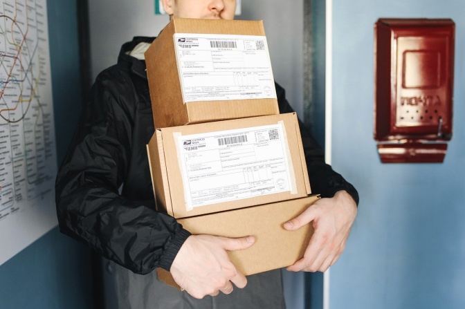 Ein Mann trägt 3 Pakete mit Adressaufklebern durch ein Treppenhaus.
