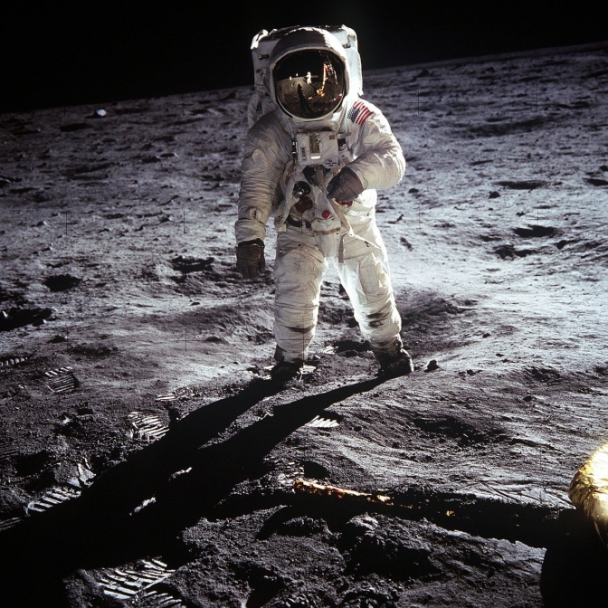 Ein Astronaut auf dem Mond. Er trägt einen weißen Weltraumanzug und einen Helm mit spiegelndem Visier