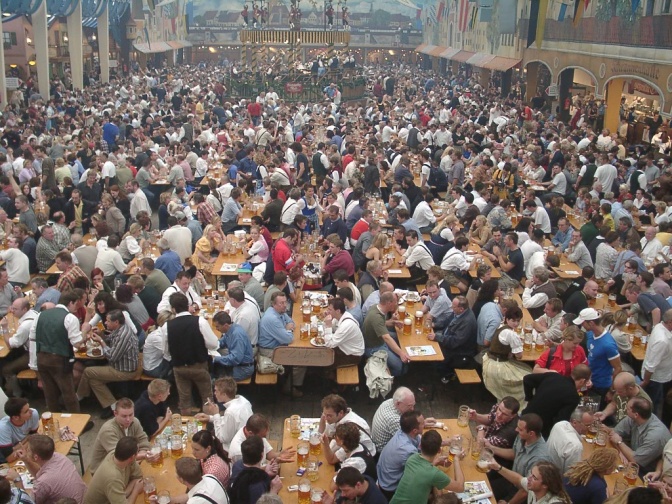 Menschen in Bierzelten beim Oktoberfest. Sie haben große Bierkrüge vor sich stehen. Die meisten tragen bayrische Tracht.