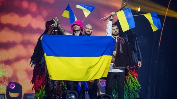 Die Mitglieder mit mehreren großen und kleinen ukrainischen Flaggen auf der Bühne