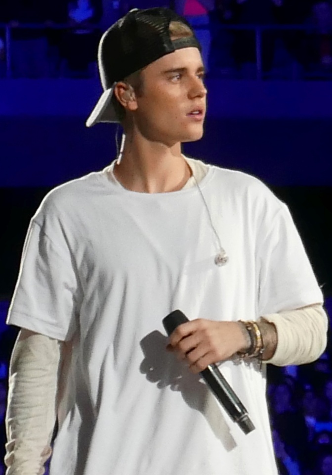 Justin Bieber in einem weißen Oversize Shirt mit nach hinten gedrehter schwarzer Schirmmütze. Er hält ein Mikro in der Hand.
