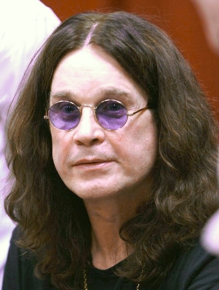 Ozzy Osbourne mit schulterlangen, gewellten braunen Haaren. Er trägt eine runde, lilane Sonnenbrille und ein schwarzes T-Shirt.