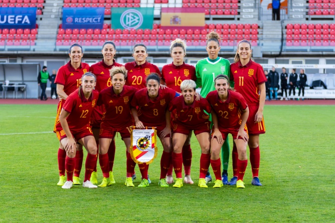 Ein Gruppenbild der spanischen Frauennationalmannschaft auf dem Feld. Alle tragen rote Trikots und stehen auf dem Feld.