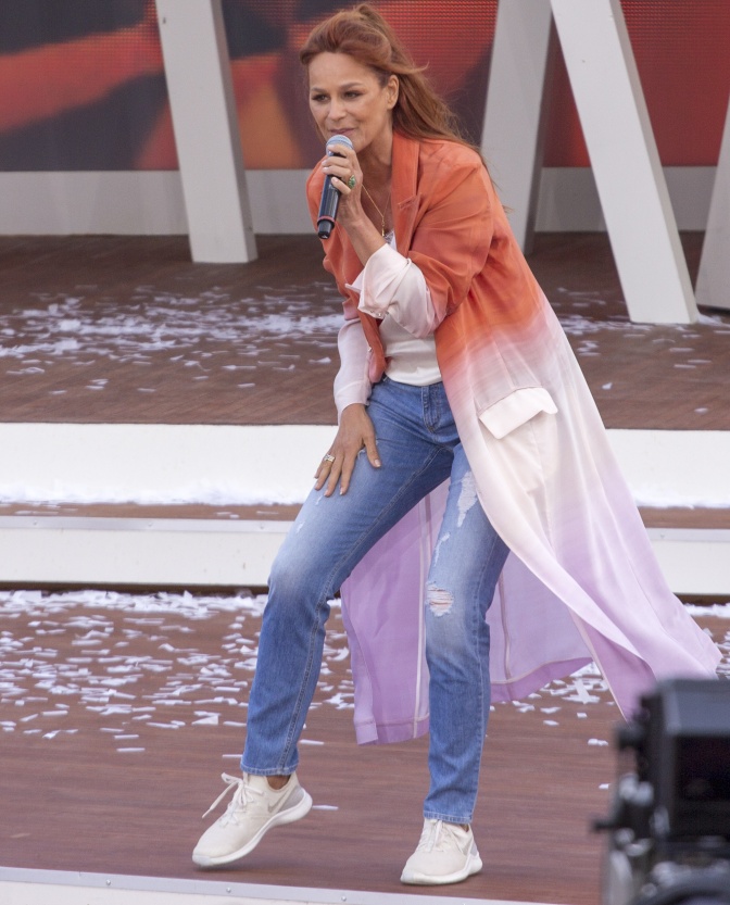 Andrea Berg steht auf der Bühne und singt in ein Mikrophon. Sie hat lange, rote Haare und trägt eine gebatikte Long-Bluse.