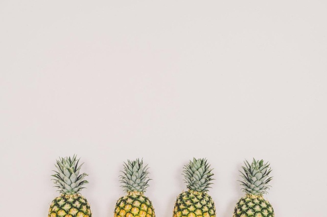 4 Ananas stehen in einer Reihe nebeneinander vor einer weißen Wand.
