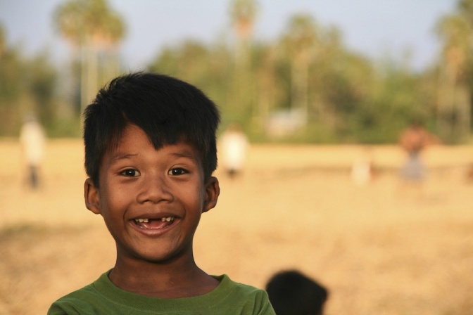 Ein Junge mit dunkler Haut und schwarzen Haaren lächelt mit einer Zahnlücke breit in die Kamera.