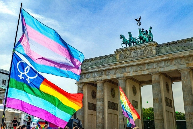Eine Regenbogenflagge und eine Transflagge wehen vor dem Brandenburger Tor