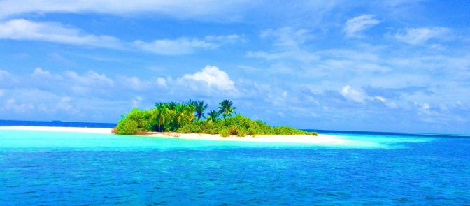 Eine kleine, mit Palmen bestandene Insel mit weißem Sand in türkis-blauem Meer