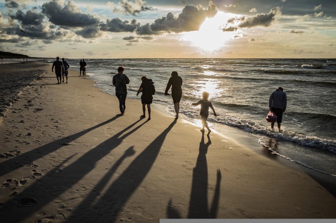 Menschen laufen an einem Strand entlang. Die Sonne wirft lange Schatten auf den Sand.