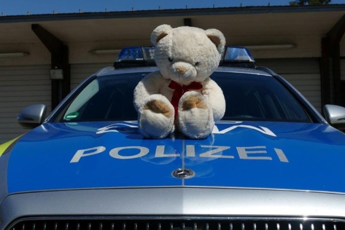 Ein großer, heller Teddybär sitzt auf der Kühlerhaube eines Polizeiautos