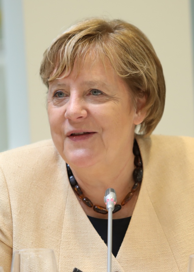 Angela Merkel in einem pfirsichfarbenen Oberteil vor einem Mikrophon
