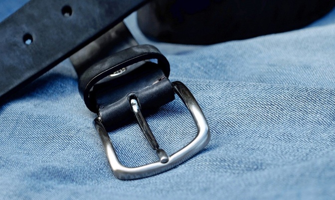 Ein schwarzer Ledergürtel mit silberner Schnalle liegt auf einer blauen Jeans.