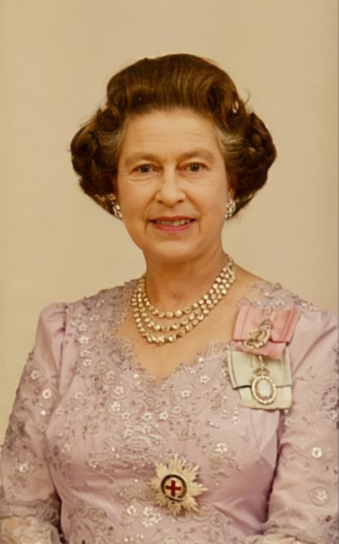 Die Queen mit braunem, in Wellen frisiertem Haar in einem festlichen rosafarbenen Kleid mit Schmuck und Orden.