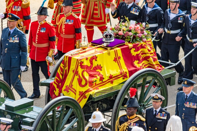 Der Sarg der Queen ist mit Flaggen bedeckt und wird von Soldaten begleitet in einer offenen Kutsche durch die Straßen Gefahren.