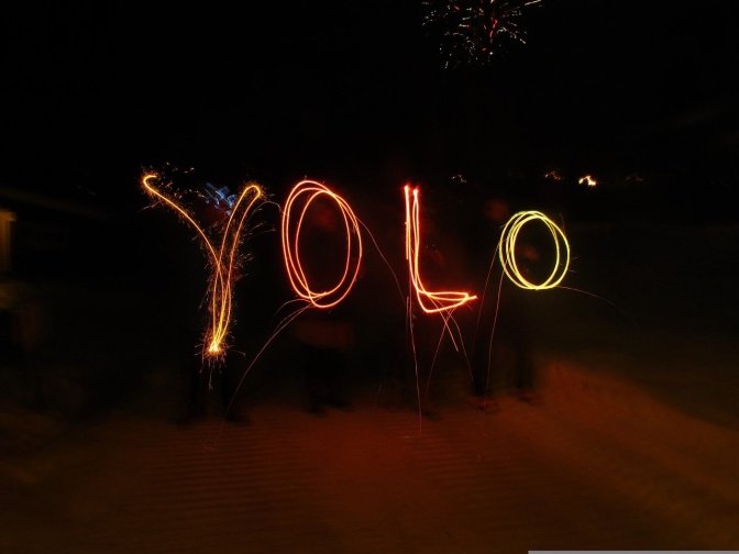Das Wort YOLO mit leuchtenden Wunderkerzen in den schwarzen Himmel geschrieben
