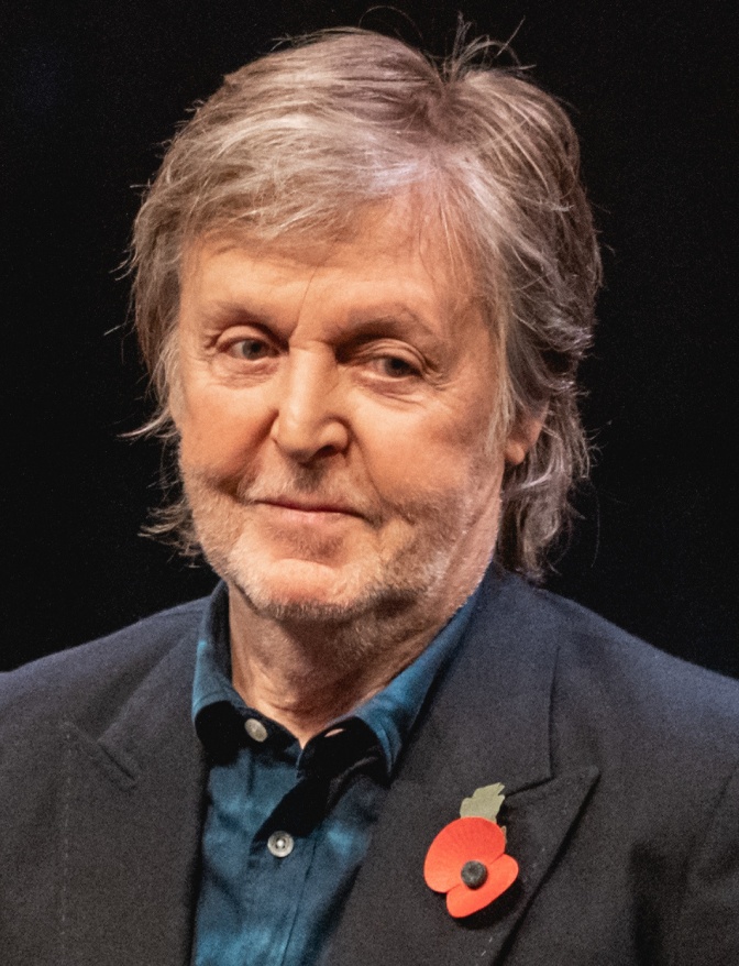Paul McCartney in Sakko und Jeanshemd. Er hat graue kurze Haare und trägt einen roten Anstecker.
