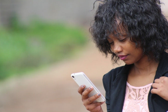 Eine dunkelhäutige junge Frau mit gewellten schwarzen Haaren schaut auf ihr Handy.