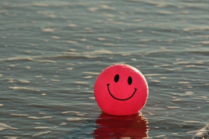 Ein pinkfarbener Ball mit Smiley-Motiv treibt auf dem Wasser.