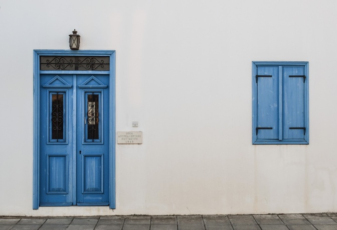 Eine blau gestrichene Tür und Fensterläden ebenfalls in blau in einer weißen Hauswand.