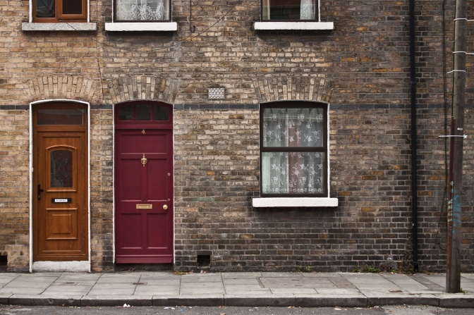 Zwei rötlich-braune Haustüren in einer geklinkten Hauswand.