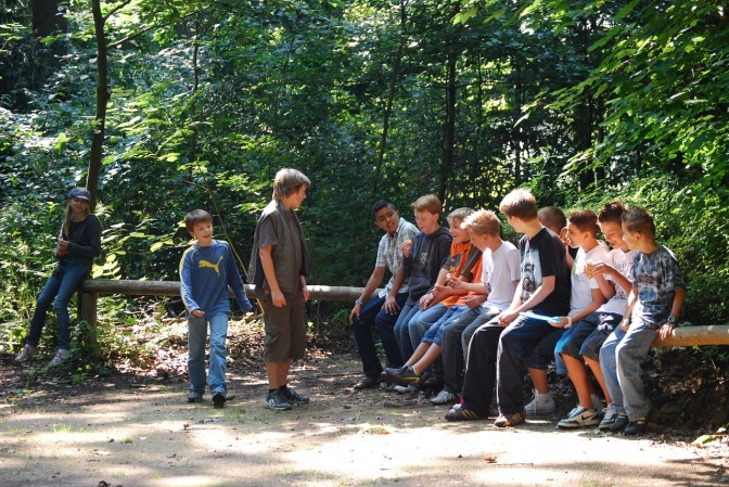 Eine Gruppe von Jugendlichen steht und sitzt im Freien zusammen und unterhält sich.