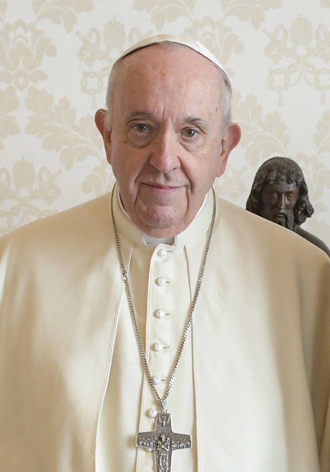 Papst Franziskus in weißer Kleidung mit einer kleinen Kappe auf dem Kopf und einer Kette mit einem großen Kreuz um den Hals.