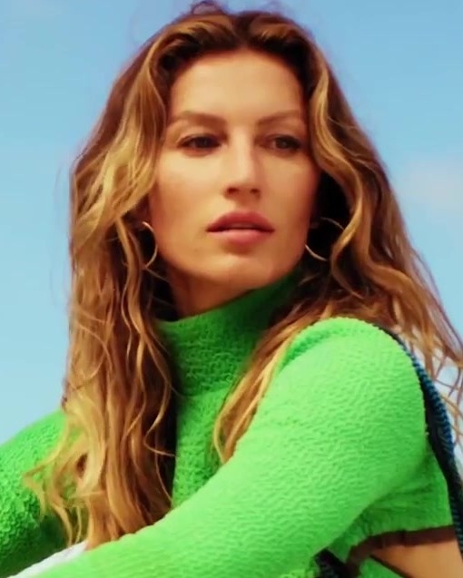 Gisele Bündchen in einem neongrünen Oberteil mit Rollkragen und mit langen, gewellten dunkelblonden Haaren.