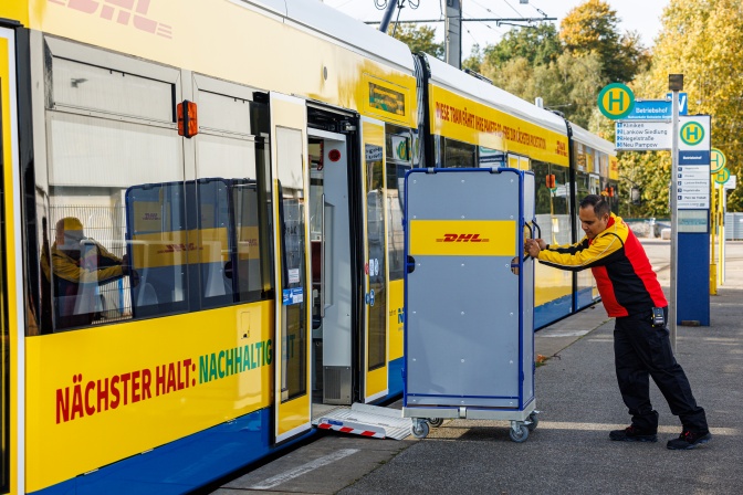 Ein Paketbote schiebt einen Wagen mit Paketen in eine Straßenbahn der DHL
