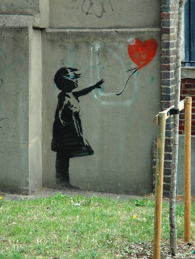 Die Silhouette eines kleinen Mädchens in schwarz, das einen roten, herzförmigen Luftballon fliegen lässt.