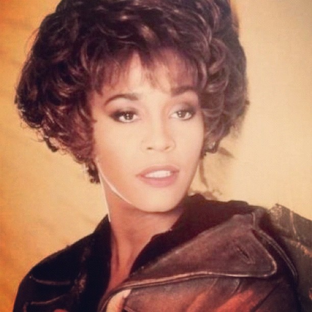Whitney Houston mit kinnlangen, gewellten braunen Haaren und hellbrauner Haut. Sie schaut seitlich an der Kamera vorbei.