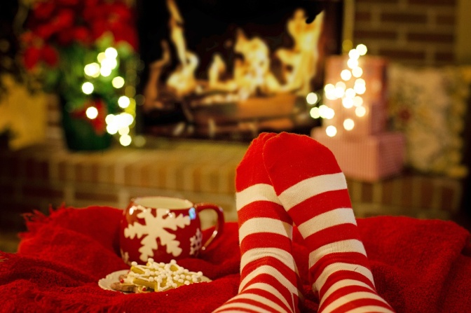Eine Person in rot-weiß geringelten Socken liegt auf der Couch. Im Hintergrund sieht man offenes Feuer im Kamin.