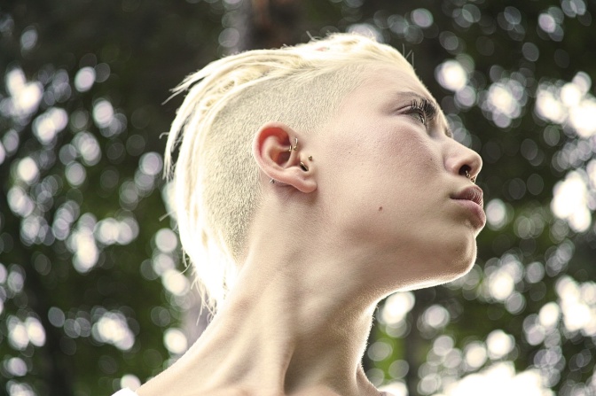Eine junge Frau mit weißblonden Haaren und Undercut. Sie hat mehrere Piercings im Gesicht.