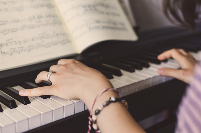 Die Hände einer Pianistin am Klavier, im Hintergrund sieht man ein aufgeschlagenes Notenheft.