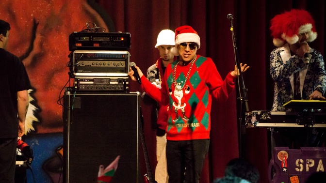 Ein Mann im Weihnachtspullover mit Weihnachtsmütze auf der Bühne