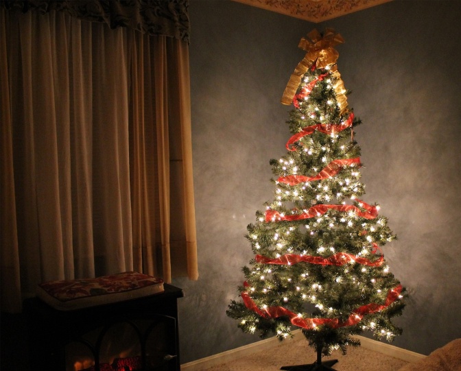 Ein geschmückter, künstlicher Weihnachtsbaum steht neben einem senffarbenen Vorhang aus Samt.