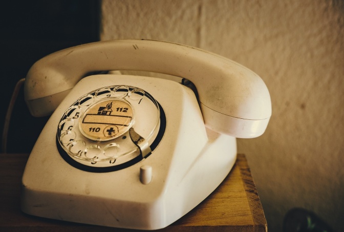 Ein altes cremefarbenes Festnertztelefon mit Wählscheibe. Auf der Wählscheibe sind die Notrufnummern 110 und 112 aufgedruckt.
