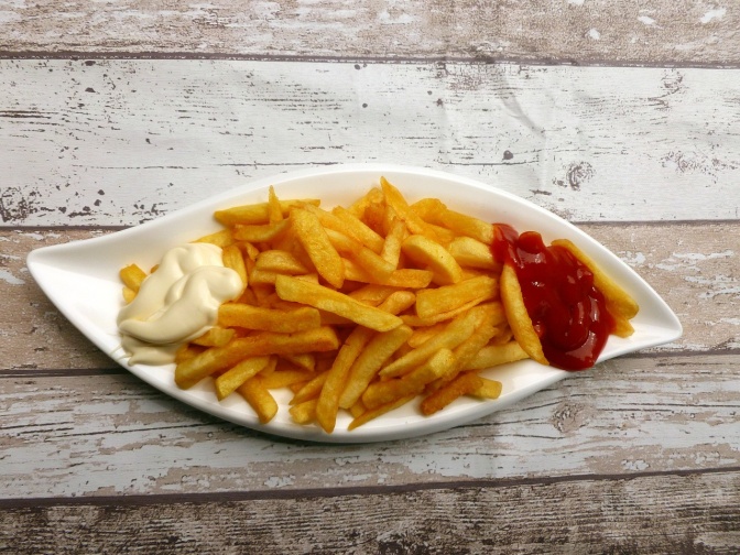 Eine Schale mit Pommes, rechts auf der Schale Ketchup, links Mayonnaise.