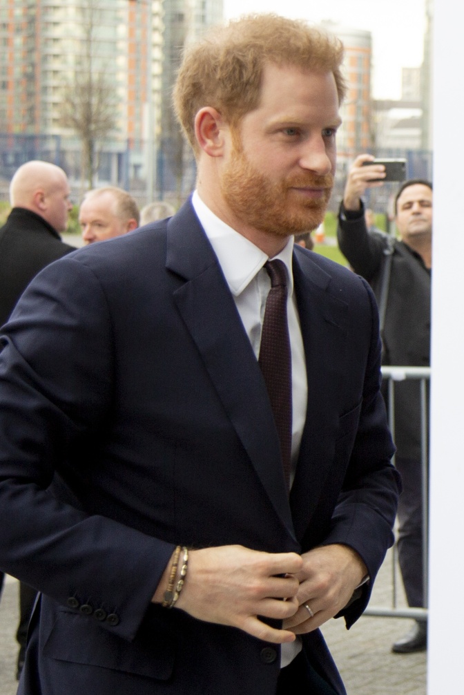 Prinz Harry mit roten Haaren und rotem Vollbart. Er knöpft sich im Laufen das Sakko zu.