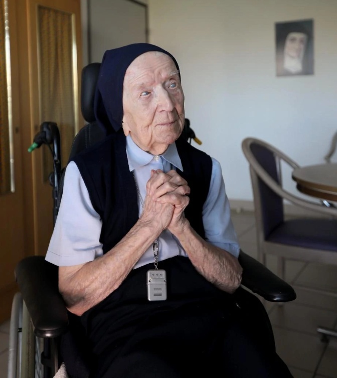 Eine alte Frau in Nonnentracht faltet die Hände vor dem Körper und betet.