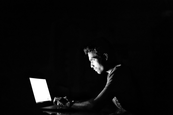 Schwarz-weiß Fotos eines Mannes, der in einem dunklen Raum vor einem Laptop sitzt.