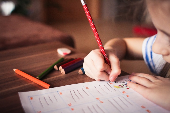 Ein Kind malt Herzen mit Buntstiften auf Papier.