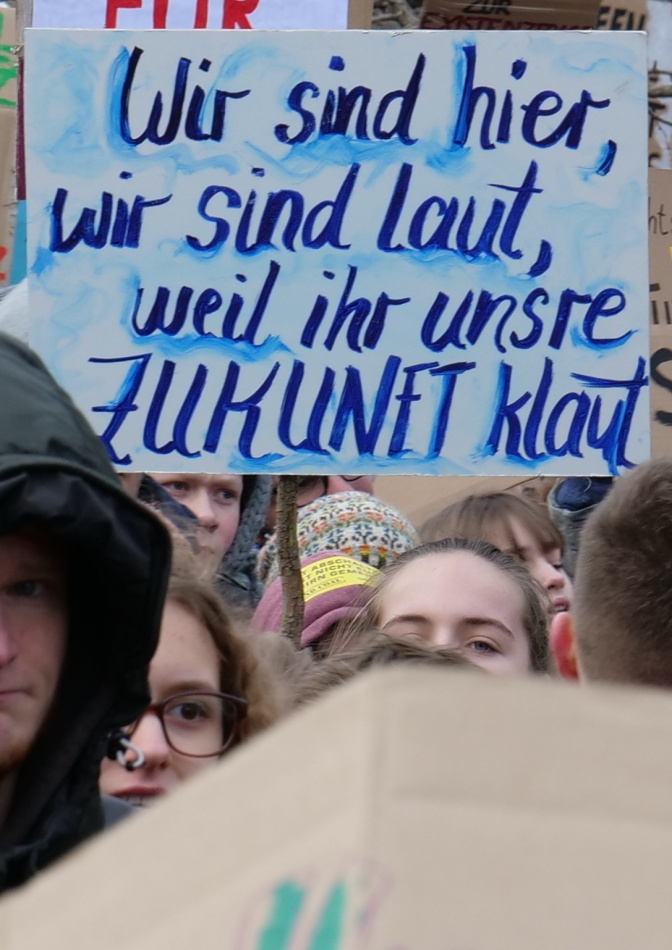 Schüler*innen tragen bei einer Demo ein Schild mit der Aufschrift: Wir sind hier, wir sind laut, weil ihr unsere Zukunft klaut.